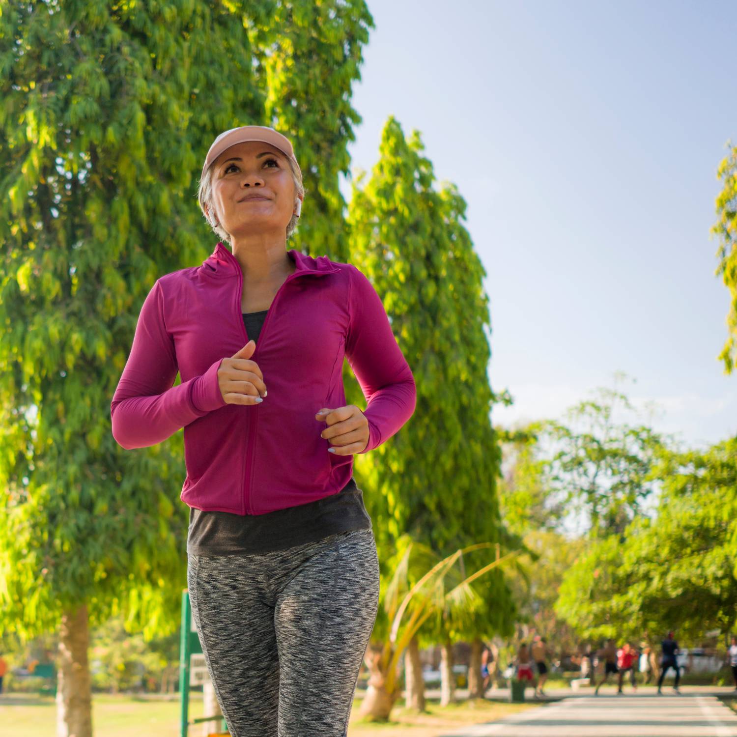 A middle-aged woman in a pink workout shit running through a city park on a sunny day.