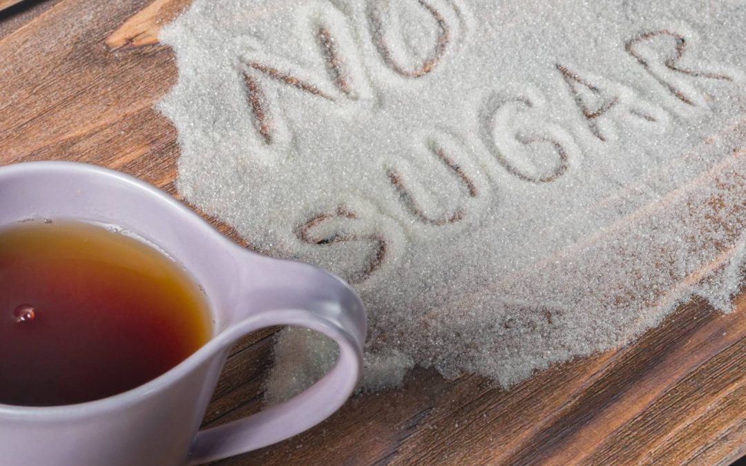 A wooden table with a cup of coffee sitting on it next to a pile of sugar with the words, "No sugar," written in it.