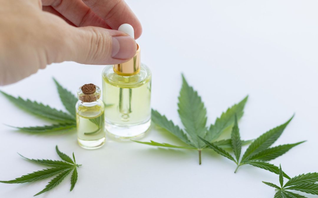 A woman’s hand holding the top of a cannabis oil bottle on a table. Cannabis leaves and a smaller bottle are on the table.