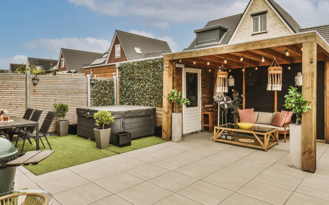 A partially covered patio with a seating area, plants, and string lights. The well-kept yard has a table, grill, and hot tub.