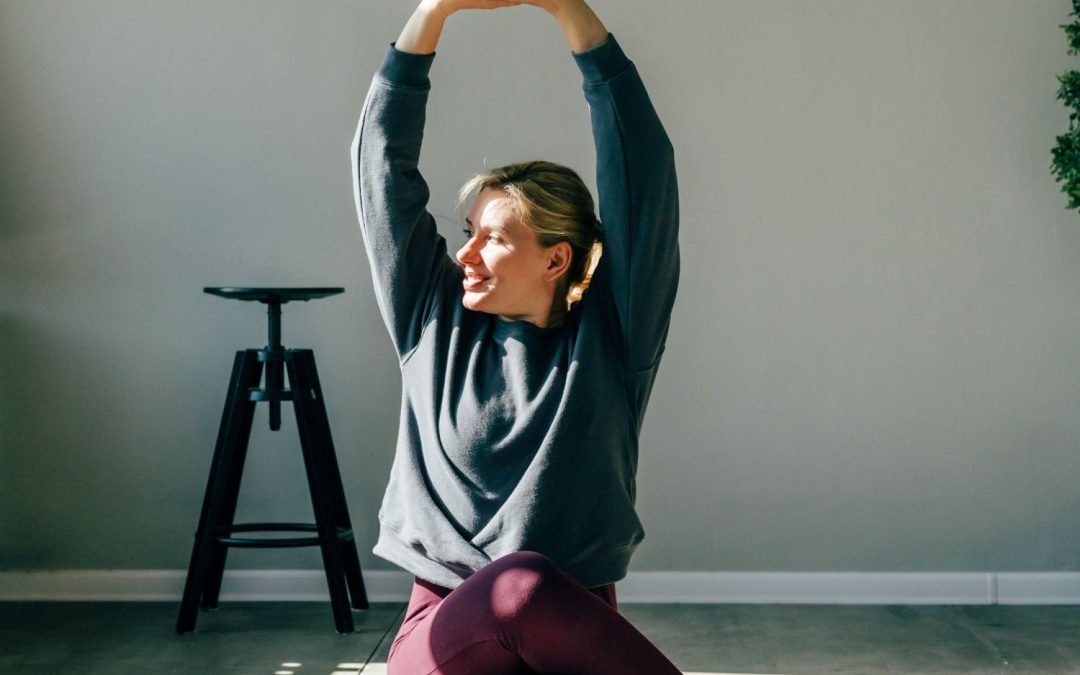 A blonde-haired woman wearing green and red workout gear is stretching and meditating during her lunch break.